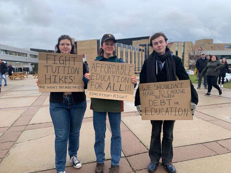 Three students holding protest signs. 