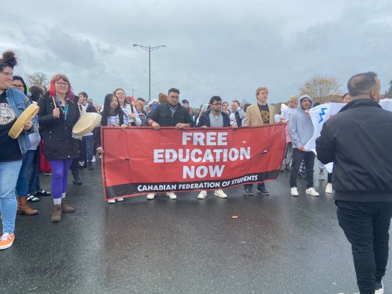 A group of students walking, holding a sign which reads 'free education now.'