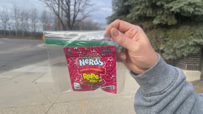 A hand holds up a bag of cannabis edible candies wrapped in a plastic bag.