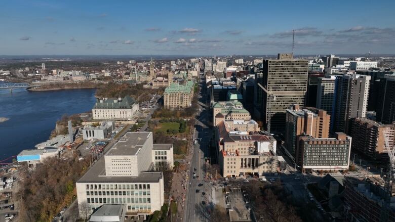 An aerial shot of a city skyline in daytime with many tall buildings and a river to the left.