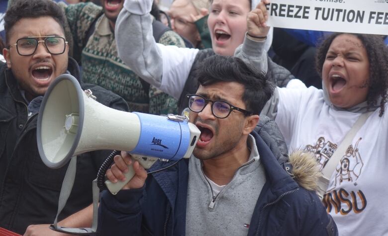 A man yells into a megaphone, surrounded by yelling protesters.