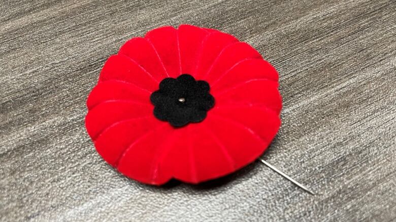 A red and black felt flower with a pin lays on a table.