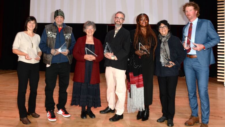 Seven people on stage smiling after an awards ceremony.