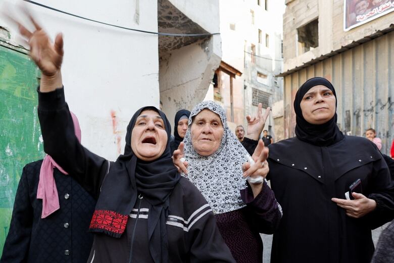 Three indivduals, all wearing headscarves, one with an arm raised. 