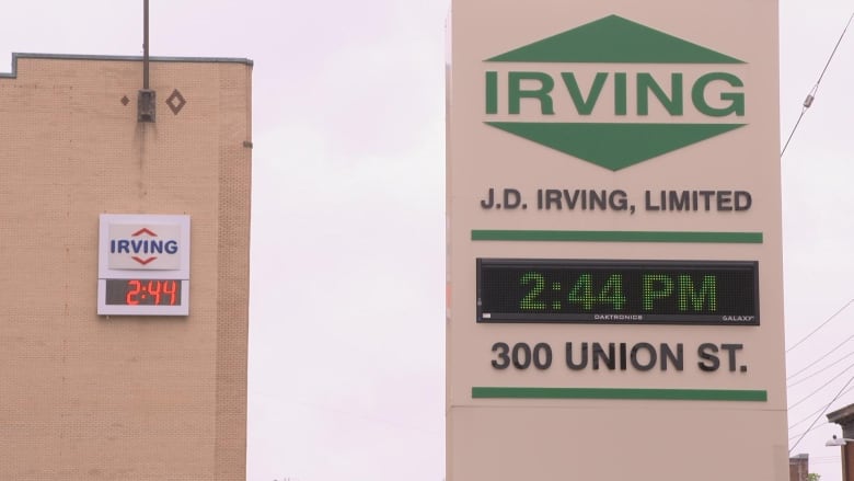 Two signs above two digital clocks are seen on nearby buildings. On the left, the red and blue logo of Irving Oil is seen. On the right is the sign for J.D. Irving, which simply says 