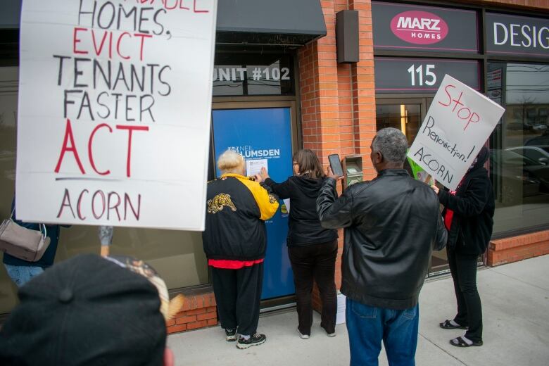 People with signs stand behind two people taping a letter onto a door.