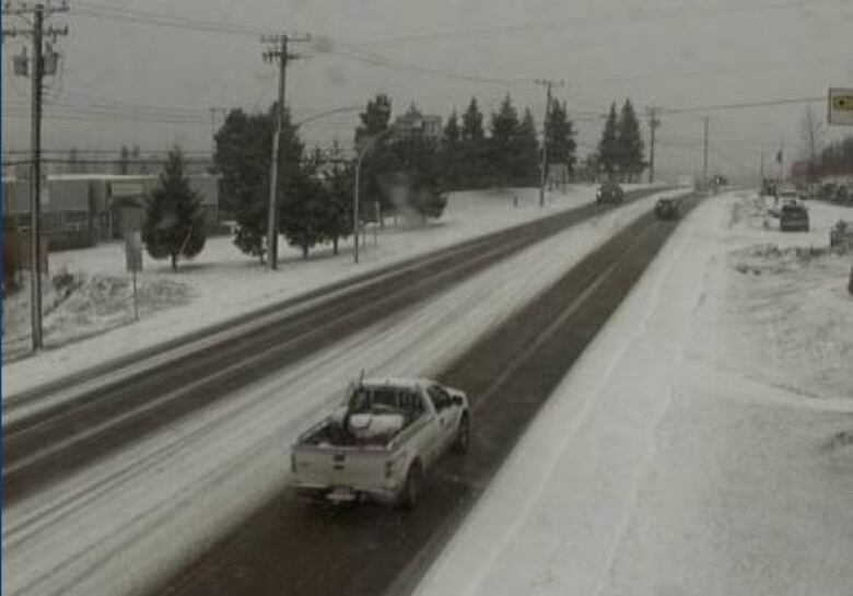 A white pick-up truck drives on a double-lane highway where snow lines both sides of the road.