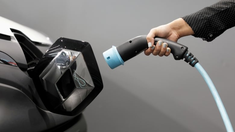 A woman holds a cable to charge an electric utility vehicle.