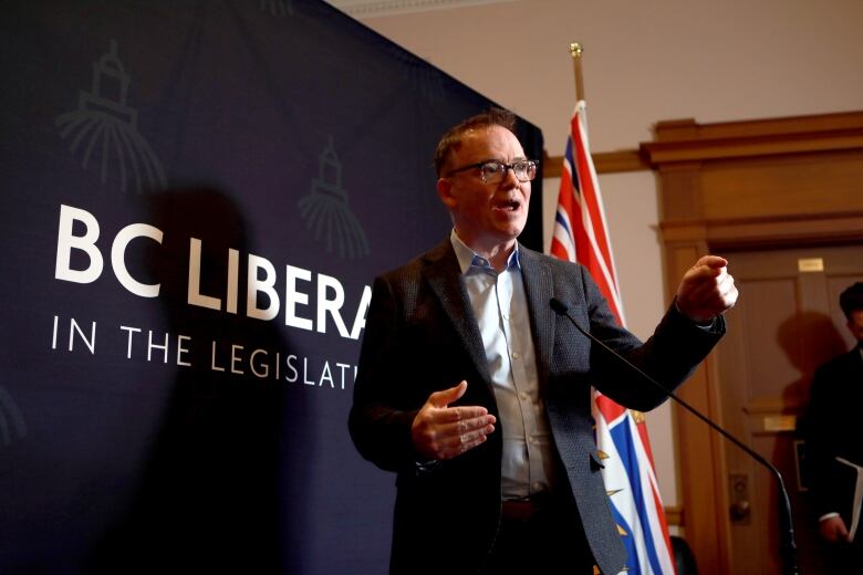 Kevin Falcon gestures at a podium. He is a white man wearing a suit and glasses.