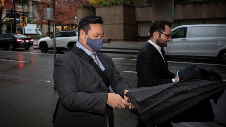 A man in a cloth mask opens an umbrella on a city street.