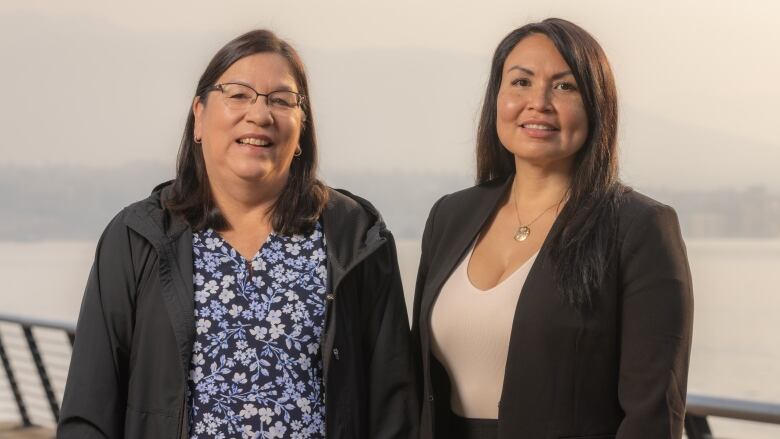 Two Indigenous women pose in front of a sea.