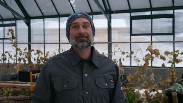 A bearded man stands posing inside a greenhouse.