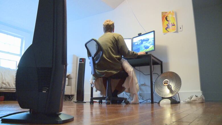 A person wearing a blanket sits at a computer.