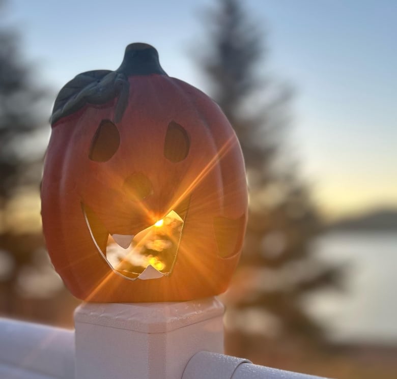 The sun shines through the mouth of a hollow jack-o-lantern placed on the post of a porch staircase.