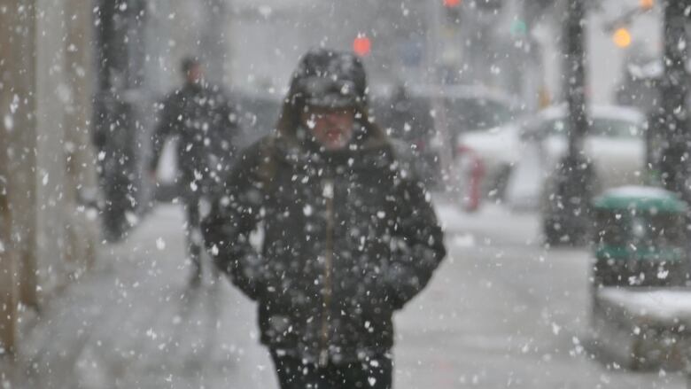 A blurred figure is seen walking along a downtown sidewalk in a heavy snowfall.