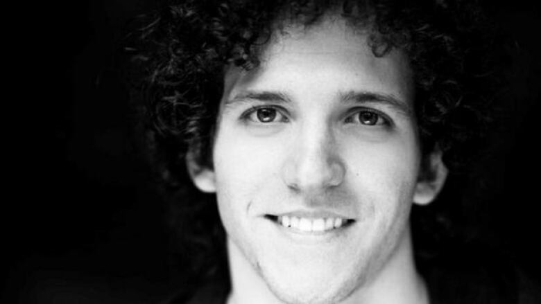 Black and white portrait of a young man with curly black hair who is smiling in front of a black background