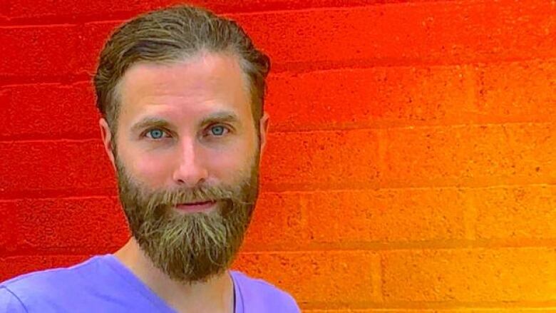 A man with light coloured hair and beard standing in front of a bright orange brick wall