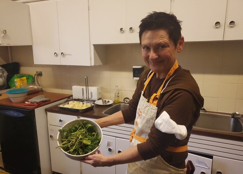 A woman with short hair smiles while holding a bowl full of freshly-harvested basil.