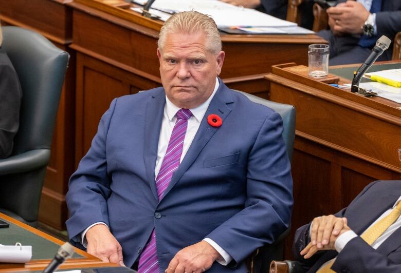 A man in a blue suit sits at a row of desks.