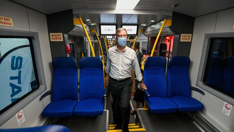 A man in a mask stands in an empty train car.