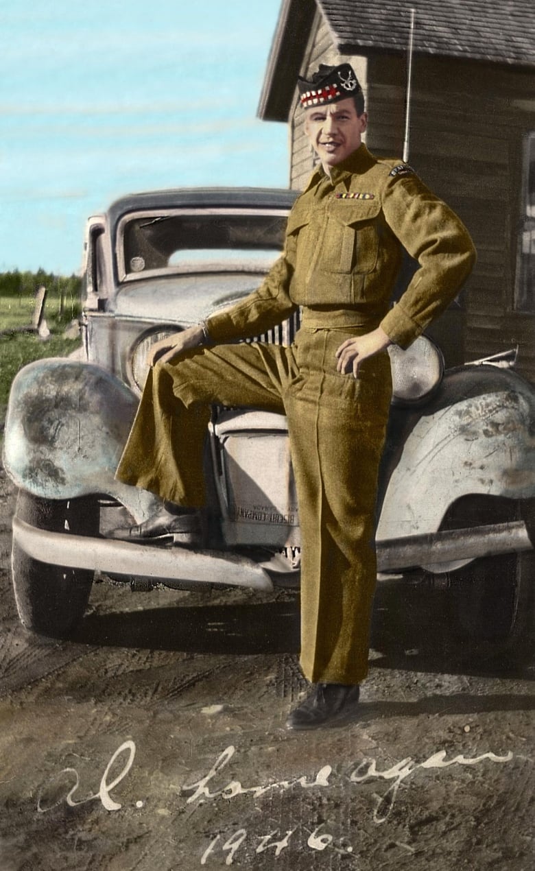 A man in green military uniform stands with his foot on the front of a car. 