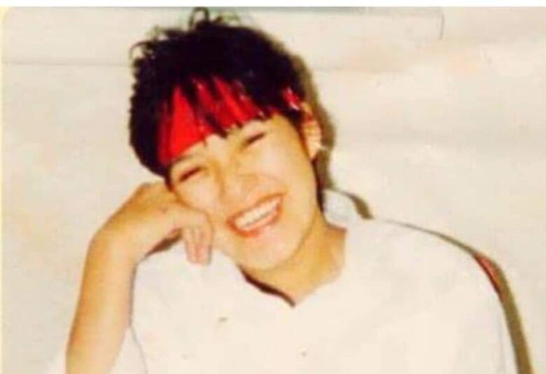 A woman wearing a red headband and a white shirt smiles and laughs at the camera.