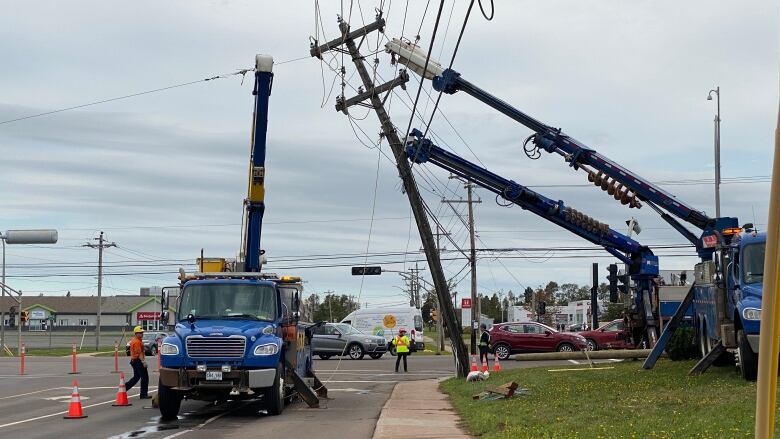 A power line is knocked partially over and two utility trucks are seen using cranes to restore it.