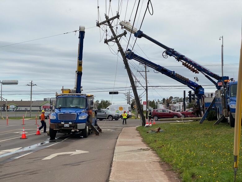 A power line is knocked partially over and two utility trucks are seen using cranes to restore it.