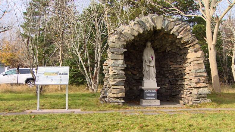 A free-standing stone grotto with a statue inside, nestled amongst trees.