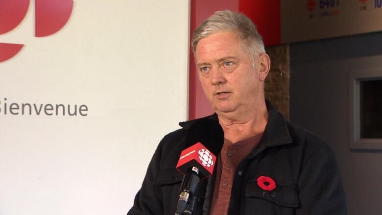 John Kennedy, a man wearing a winter coat with a poppy in the lapel, speaks to the CBC