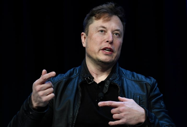 Close-up of short haired individual wearing a leather jacket, gesturing with his hands as he speaks. 