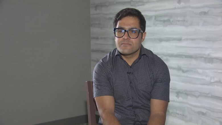 A spectacled man sits clad in a T-shirt.