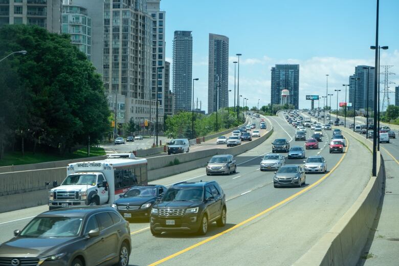 Vehicles drive along Queen Elizabeth Way in Toronto with condo buildings in the background. 