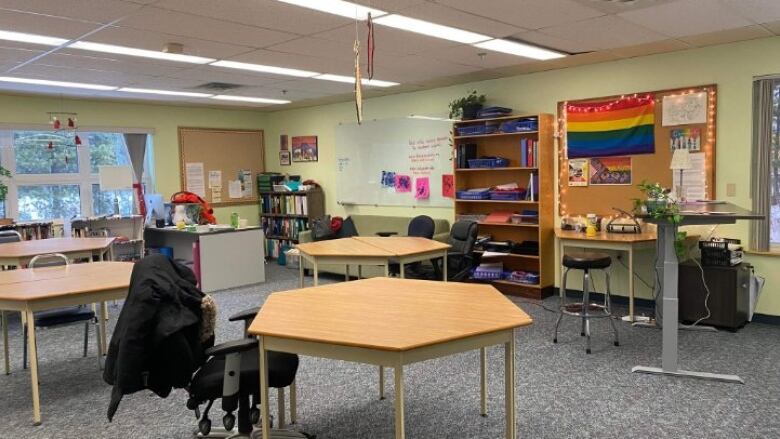 A classroom with desks, bookcases, bulletin boards and a whiteboard. A coat hangs over an empty chair.