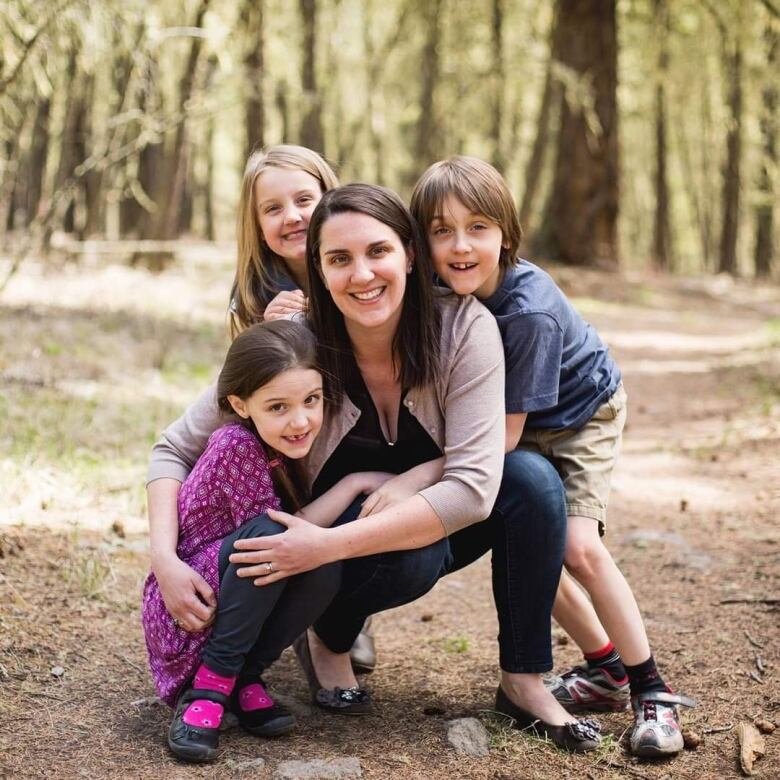 A brunette woman is surrounded by three children in a forest.