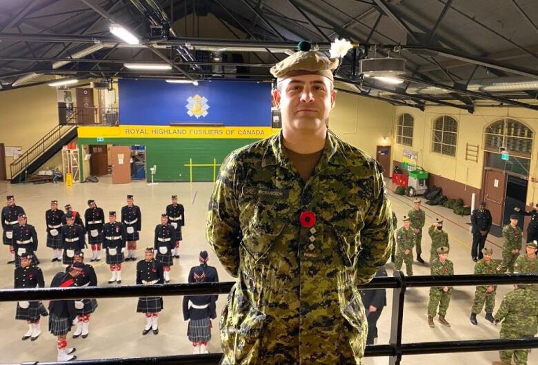 Soldier stands on a balcony over a gym where other soldiers stand at attention.