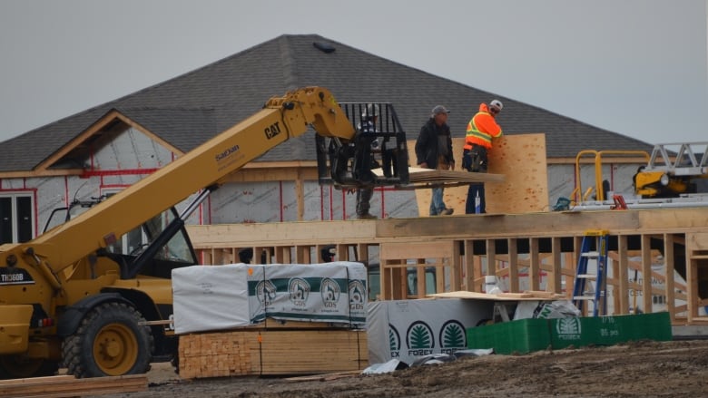 Construction workers stand on a partly built house in the Hanmer area of Greater Sudbury, surrounded by machines, piles of lumber and other houses under construction.