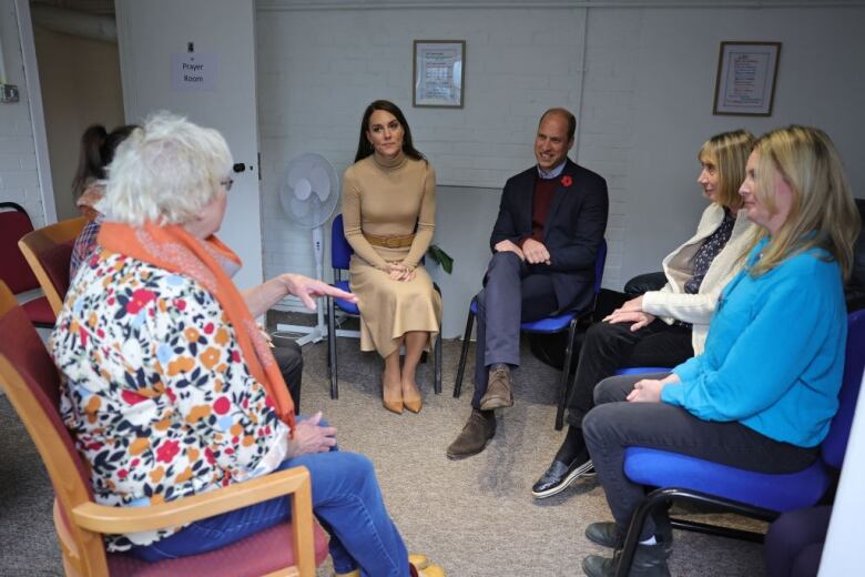 Several adults sit on chairs in a circle.