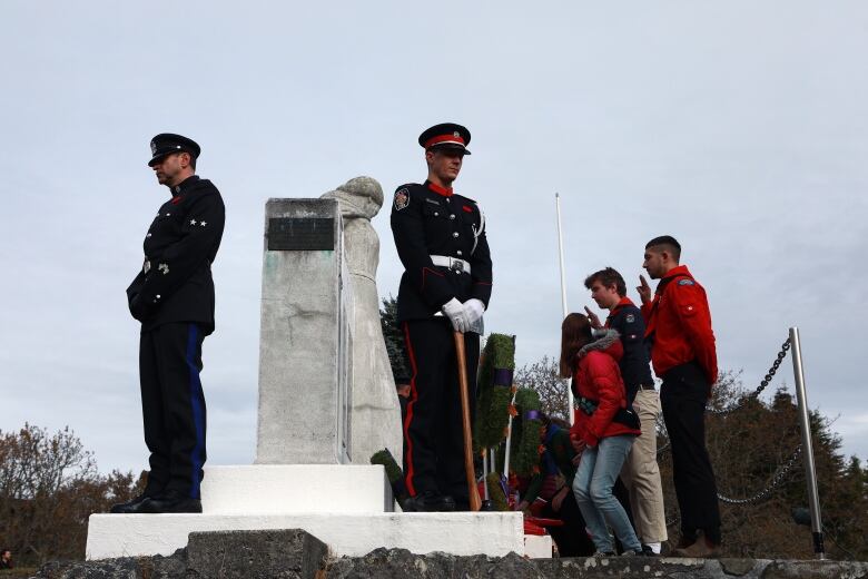 Two soldiers stand guard at a cenotaph as members of the public lay wreaths.