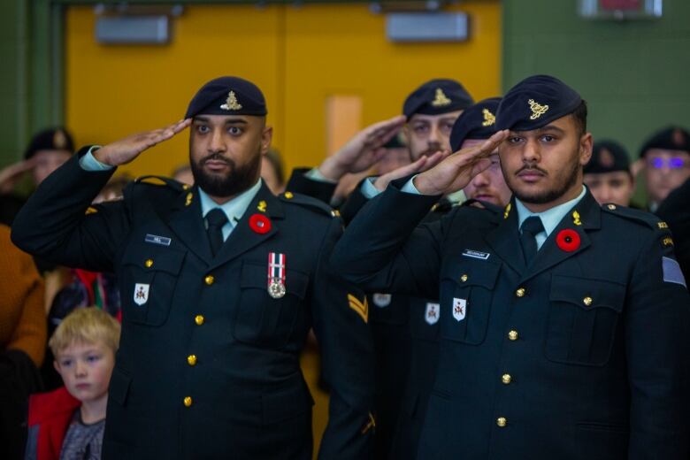 Soldiers in military dress uniforms salute wearing poppies.