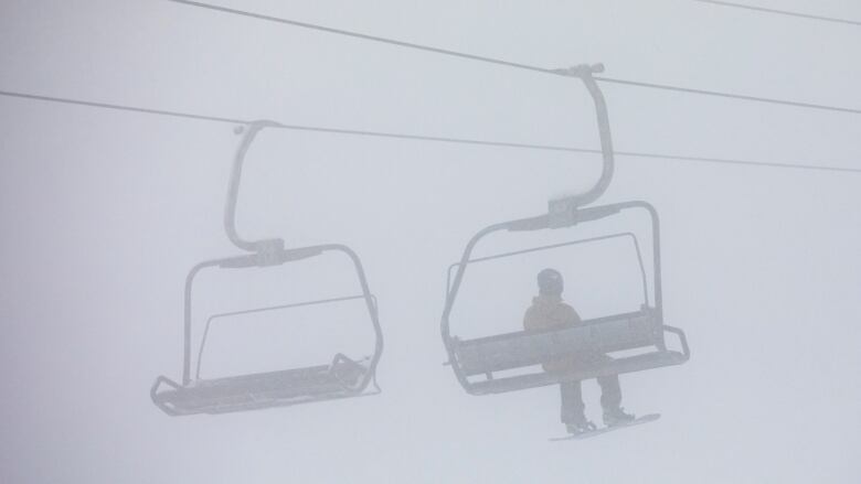 A snowboarder sits on a ski lift in hazy conditions.