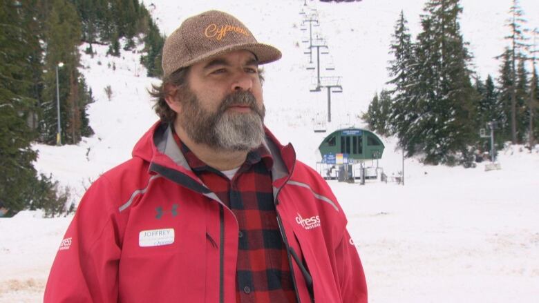 A white man wears a Cypress-branded jacket and hat in a snowy environment.