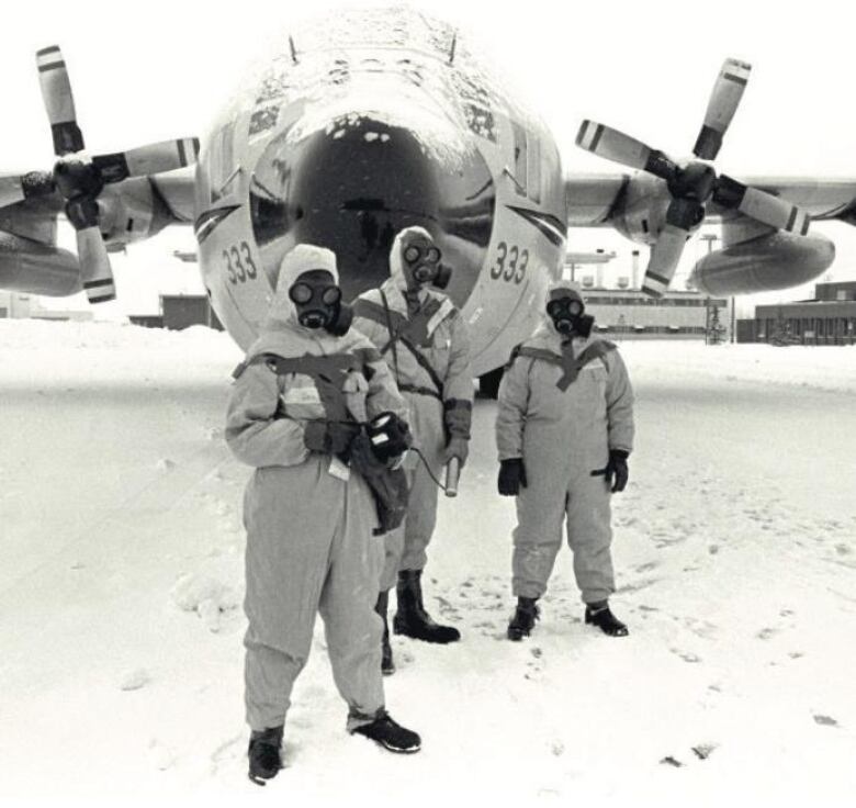 Three members of the Operation Morning Light team stand in front of an airplane in uniform, wearing gas masks.