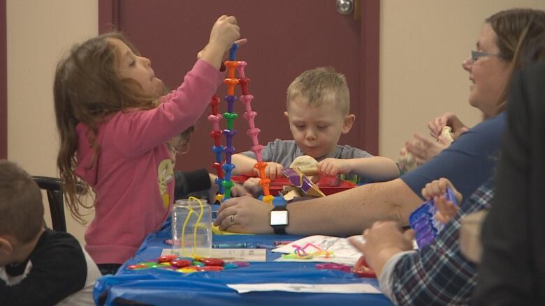 Children play with toys at a table in a daycare. Their caregiver is sitting on the right.