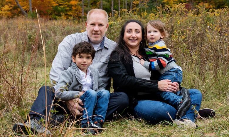 A family of four sits on grass.