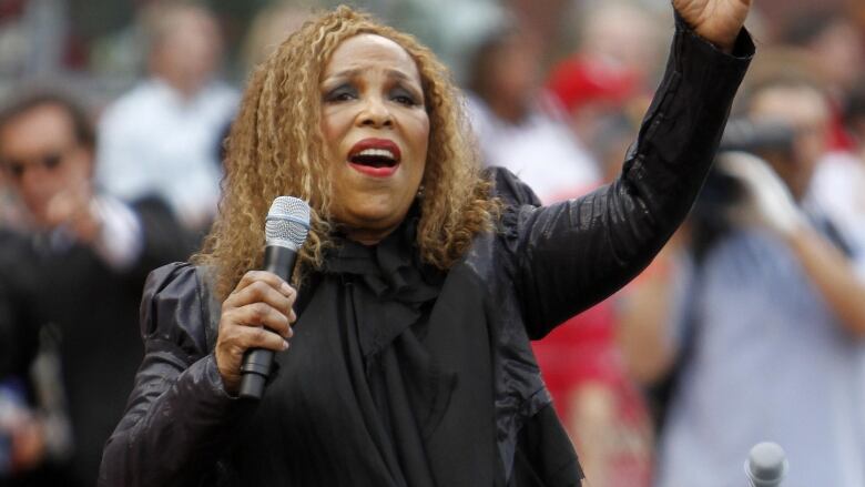 An individual with curly long hair, arm raised, singing into a microphone.