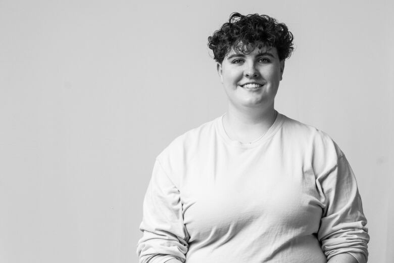 A young person with curly hair smiles at the camera in a black-and-white photo.