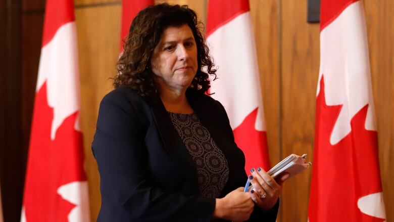 A women wearing a blue suit walks in front of a row of Canadian flags.