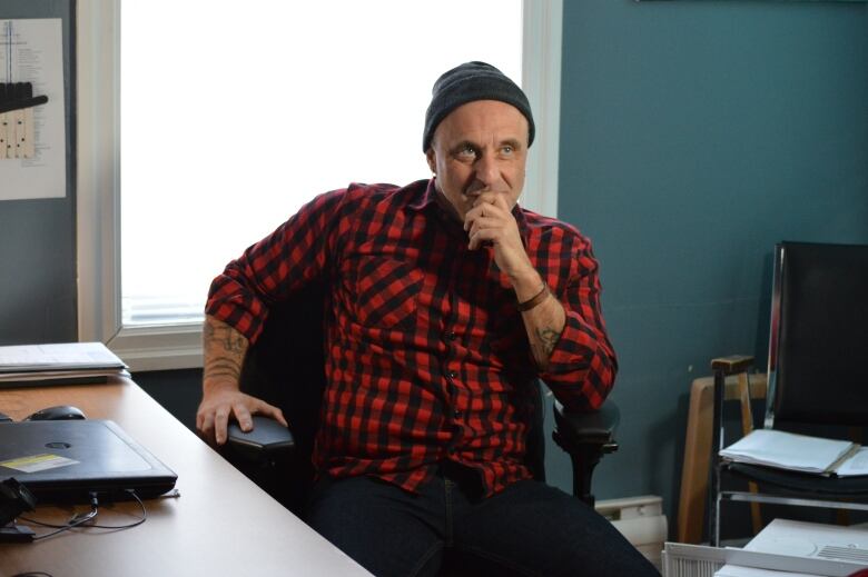 A man in a plaid shirt in an office chair with a grim look on his face