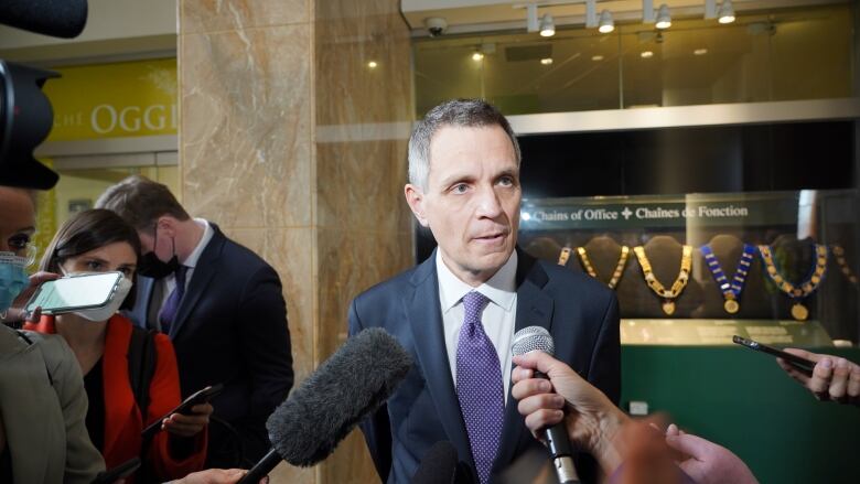 A man in a suit and tie is interviewed by several reporters.